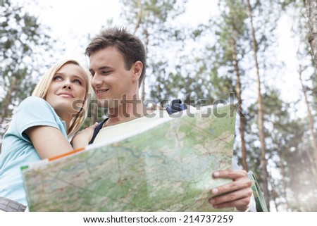 Happy young backpackers holding map in forest