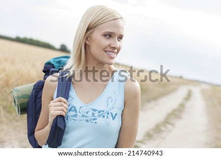 Beautiful female hiker with backpack looking away while standing on field