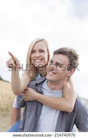 Beautiful woman showing something to man while enjoying piggyback ride at field