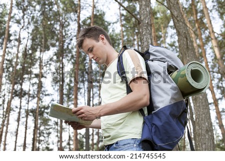 Side view of young man with backpack reading map in woods