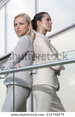 Serious young businesswomen standing back to back at office railing