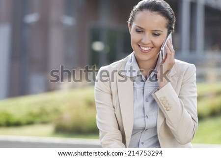 Happy young businesswoman using mobile phone while looking down outdoors