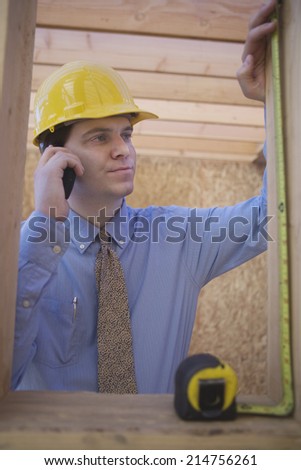 Young architect measuring a wooden beam while using cell phone at construction site