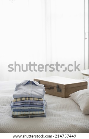 Ironed and folded shirts on bed next to suitcase in bedroom