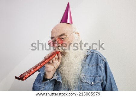 Senior man wearing party hat while blowing horn against gray background