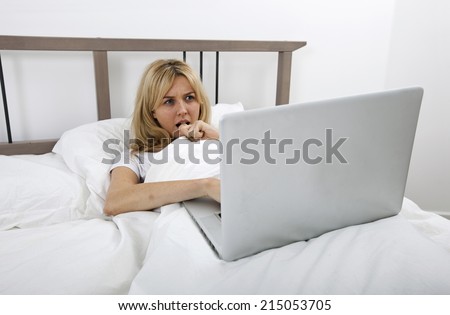 Thoughtful young woman looking at laptop in bed