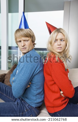 Side view of annoyed couple in Christmas sweaters and party hats sitting back to back at home