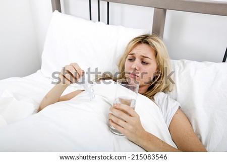 Woman suffering from cold holding water and tablet in bed
