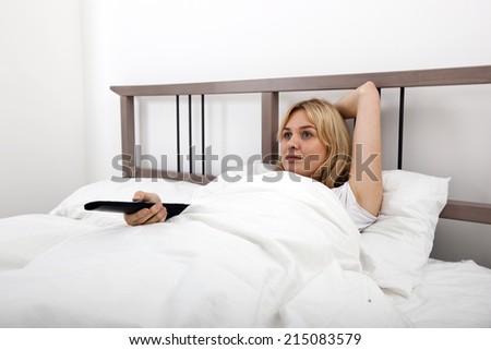 Young woman changing channels with remote control in bed