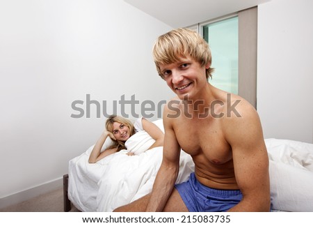 Portrait of man in underwear sitting on bed with woman looking at him