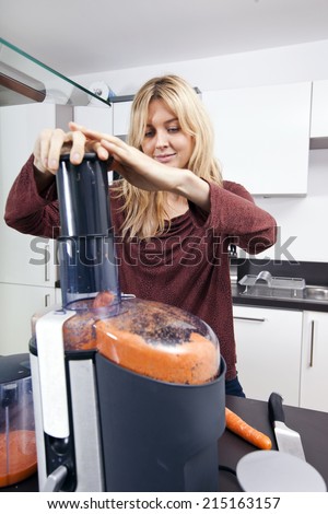 Young woman juicing carrots in kitchen