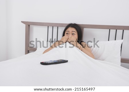 Frightened woman watching TV in bed
