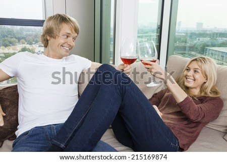 Happy relaxed couple toasting wine glasses in living room at home