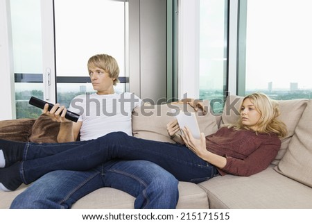 Relaxed couple reading book and watching TV in living room at home