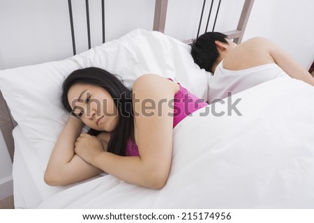 Displeased Asian woman with man sleeping in bed