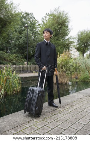 Full length of Asian businessman with luggage standing by pond