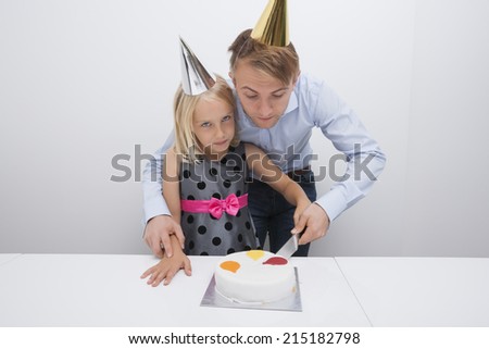 Father and daughter cutting birthday cake at table