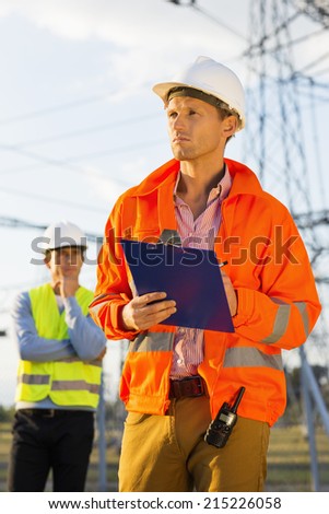 Male architect with clipboard working at site while coworker standing in background