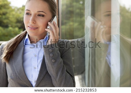 Businesswoman answering cell phone by glass door