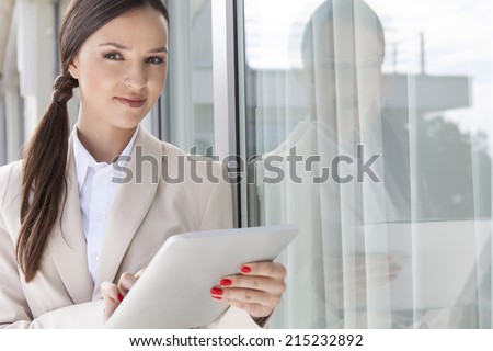 Portrait of confident businesswoman using digital tablet by glass door