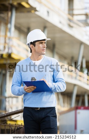 Architect with clipboard and pen working at construction site