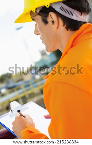 Side view of construction worker writing on clipboard at construction site