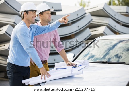 Architects with blueprints on car discussing at site