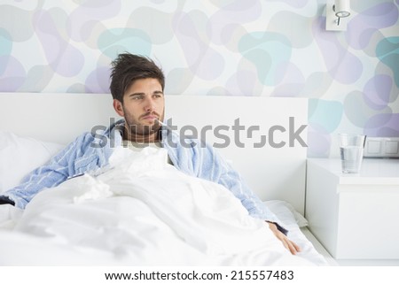 Sick man with thermometer in mouth reclining on bed at home