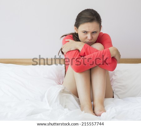 Sad woman hugging knees on bed at home