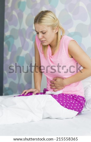 Young woman suffering from abdomen pain in bedroom