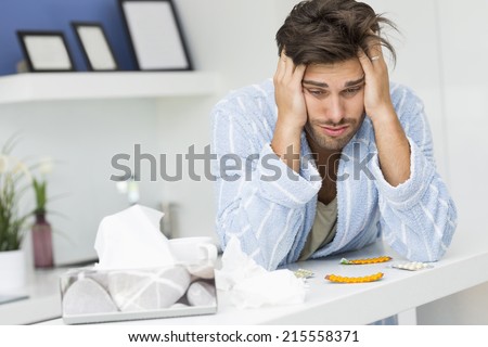 Young ill man suffering from headache at kitchen counter