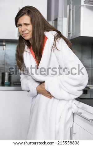 Young woman suffering from abdomen pain standing in kitchen