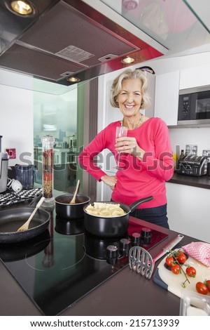 Portrait of happy senior woman with champagne glass cooking food in kitchen