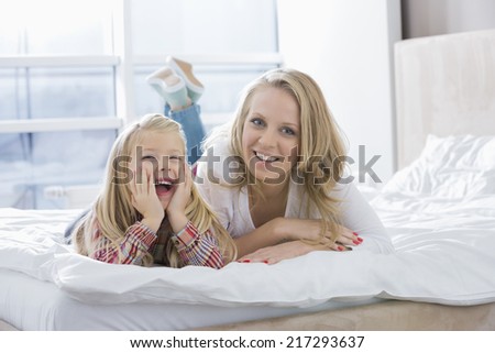 Portrait of happy mother and daughter lying in bed