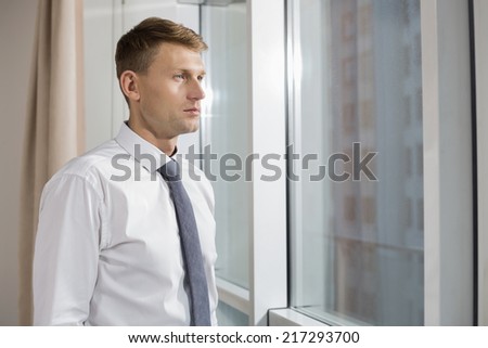 Thoughtful mid adult businessman looking through window at home