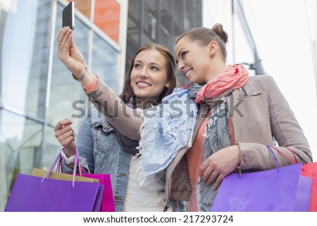 Female friends with shopping bags taking self portrait through mobile phone