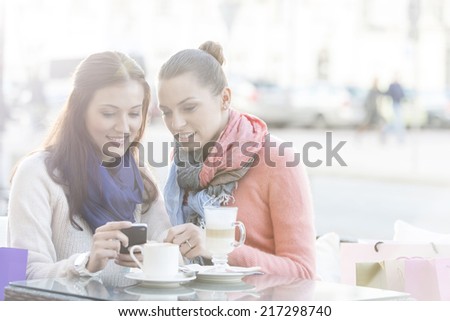 Happy women using cell phone at sidewalk cafe during winter