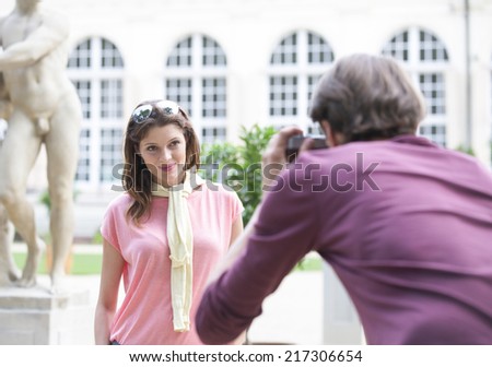 Rear view of man photographing woman against building