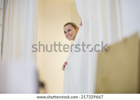Happy woman in hiding behind curtains in store