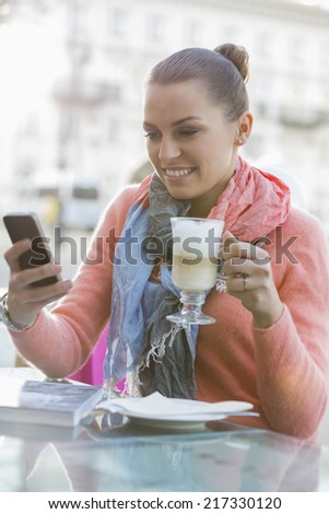 Young woman having coffee while using cell phone at sidewalk cafe