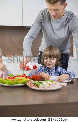 Father pouring juice for son at table in kitchen