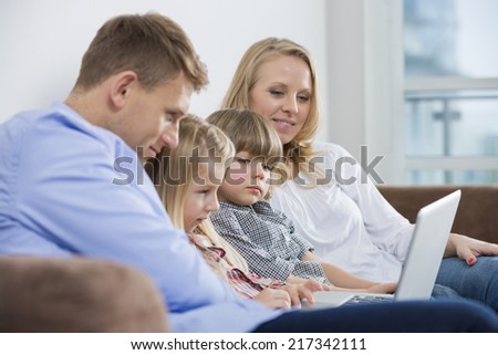 Parents with children using laptop on sofa at home
