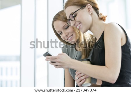 Smiling businesswomen using cell phone during break in office