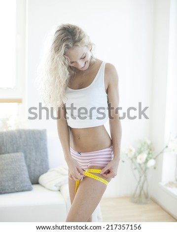 Happy woman measuring thigh with tape