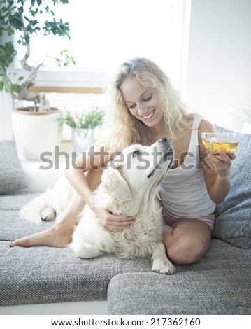 Beautiful woman holding tea cup while touching dog on sofa