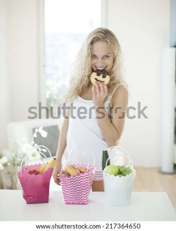 Portrait of happy woman eating cookie at kitchen counter