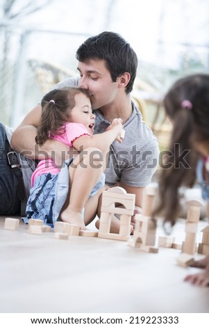 Loving father kissing daughter building blocks on floor
