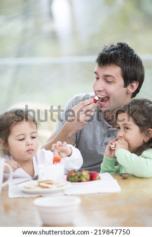 Father and daughters eating strawberries with whipped cream at home
