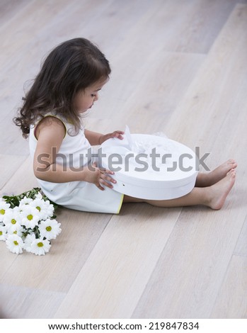Full length side of little girl opening gift box on floor at home