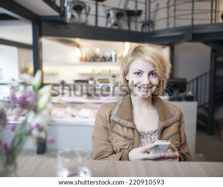 Portrait of happy young woman using cell phone in cafe
